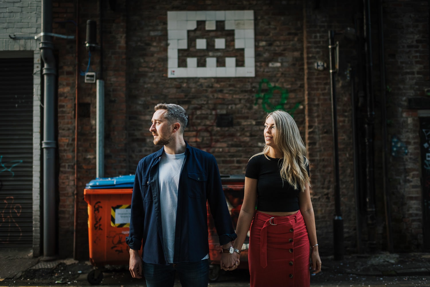 A couple holding hands in front of a space invaders tile mural