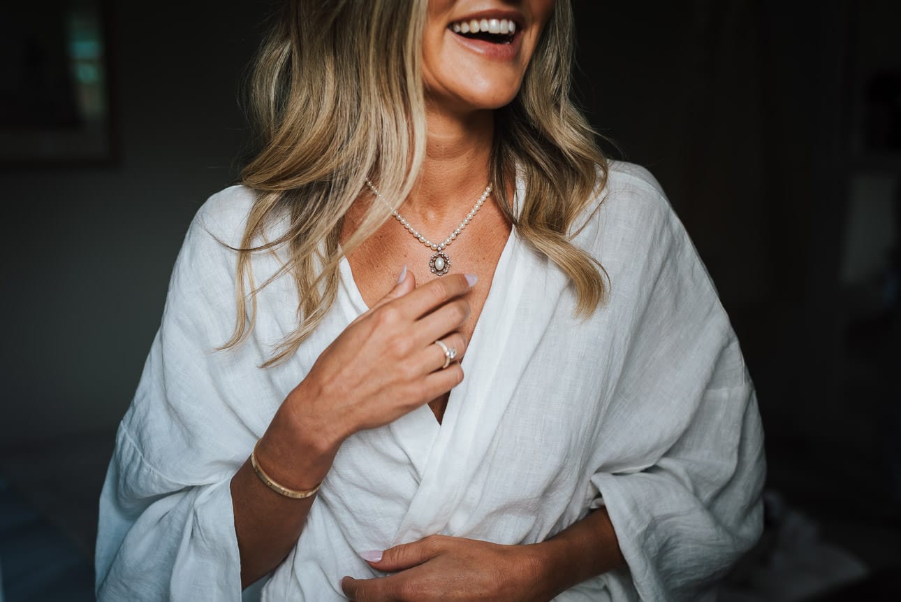 A London bride in pyjamas putting on her necklace