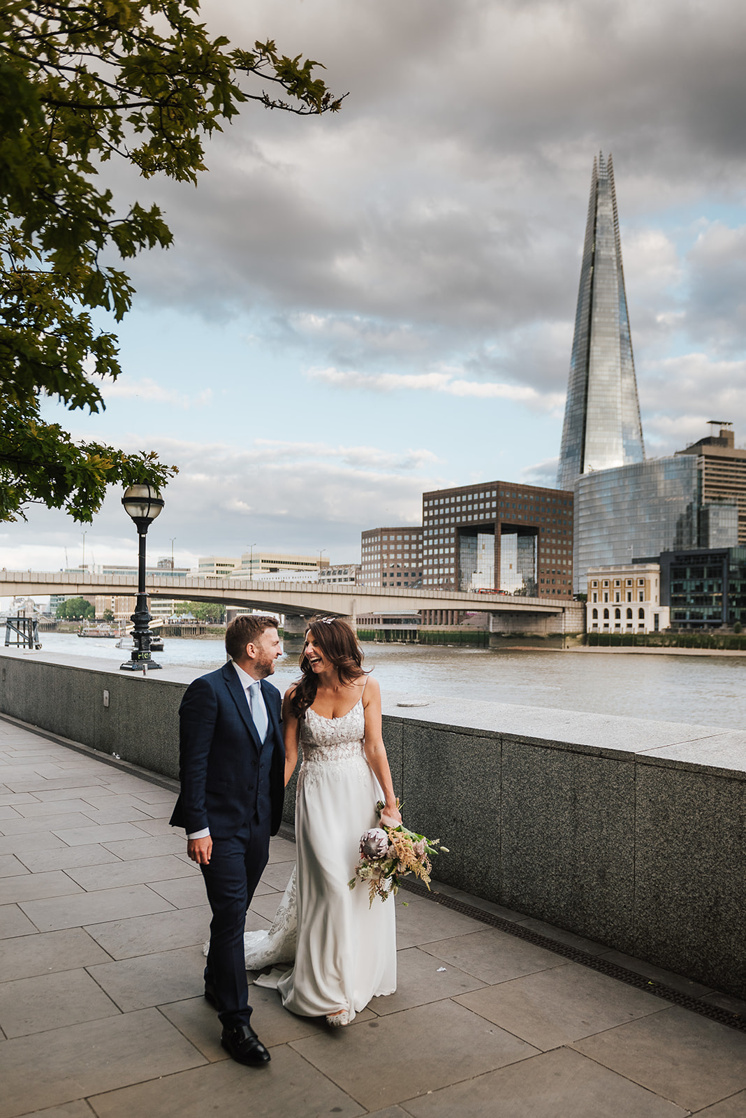 A bride and Groom walking on the banks of the Thames near the Shard