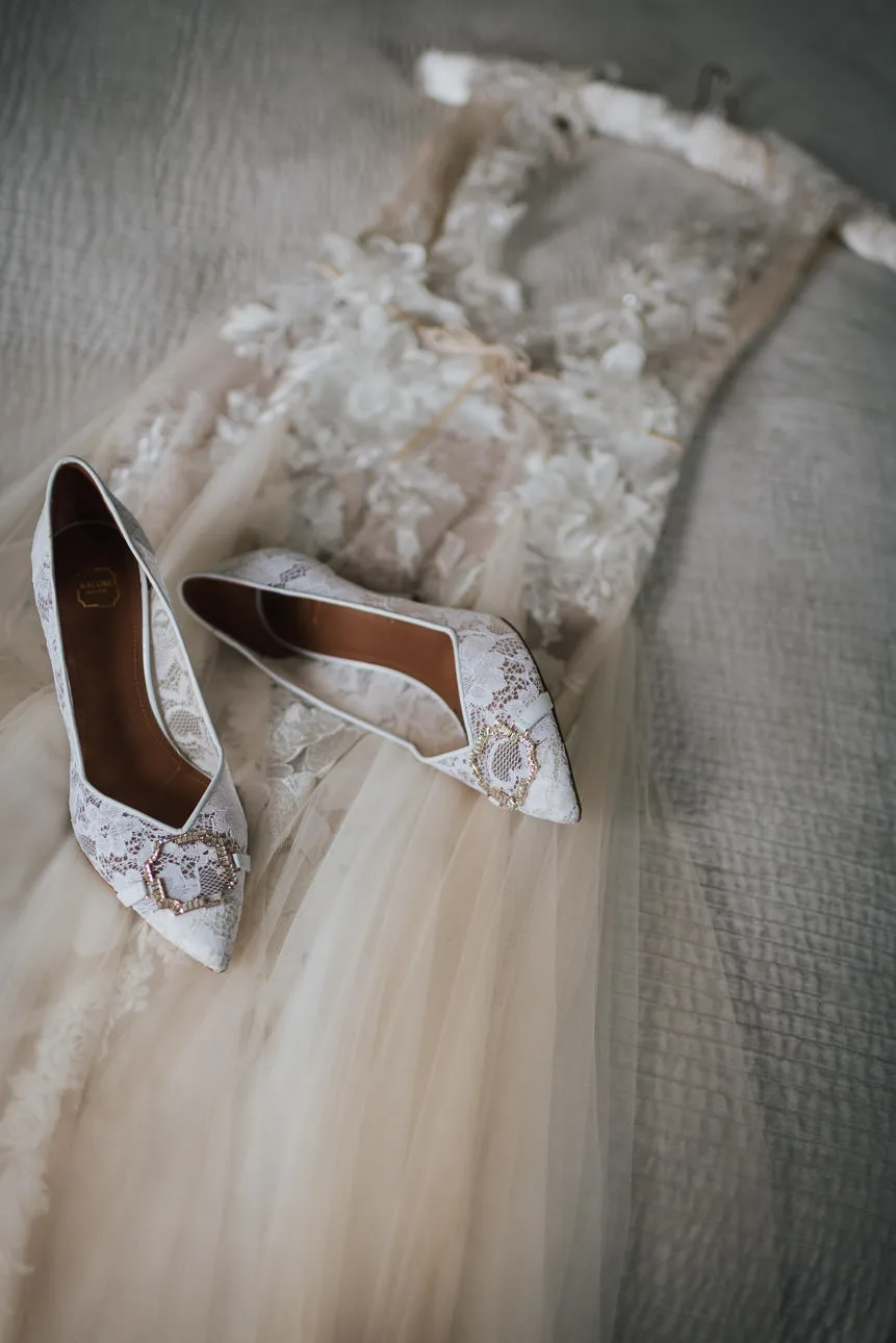 A beautiful lace wedding dress and wedding shoes on a bed