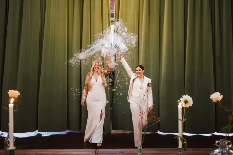 A bride and her bride walking into their wedding with bubble guns