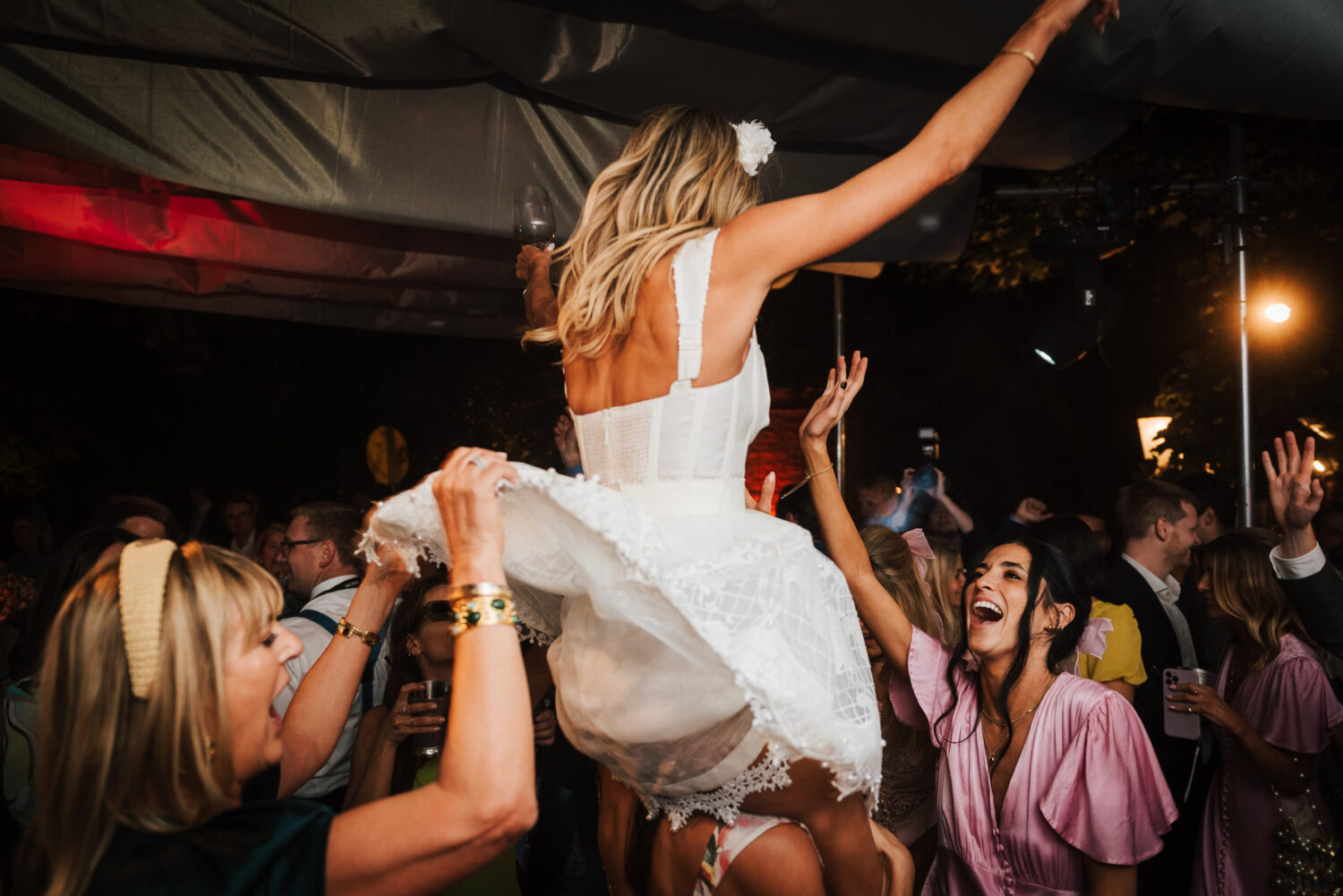 A bride in white being lifted on the crowds shoulders and dancing