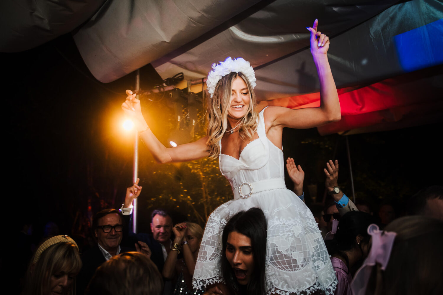 A bride in white being lifted on the crowds shoulders and dancing