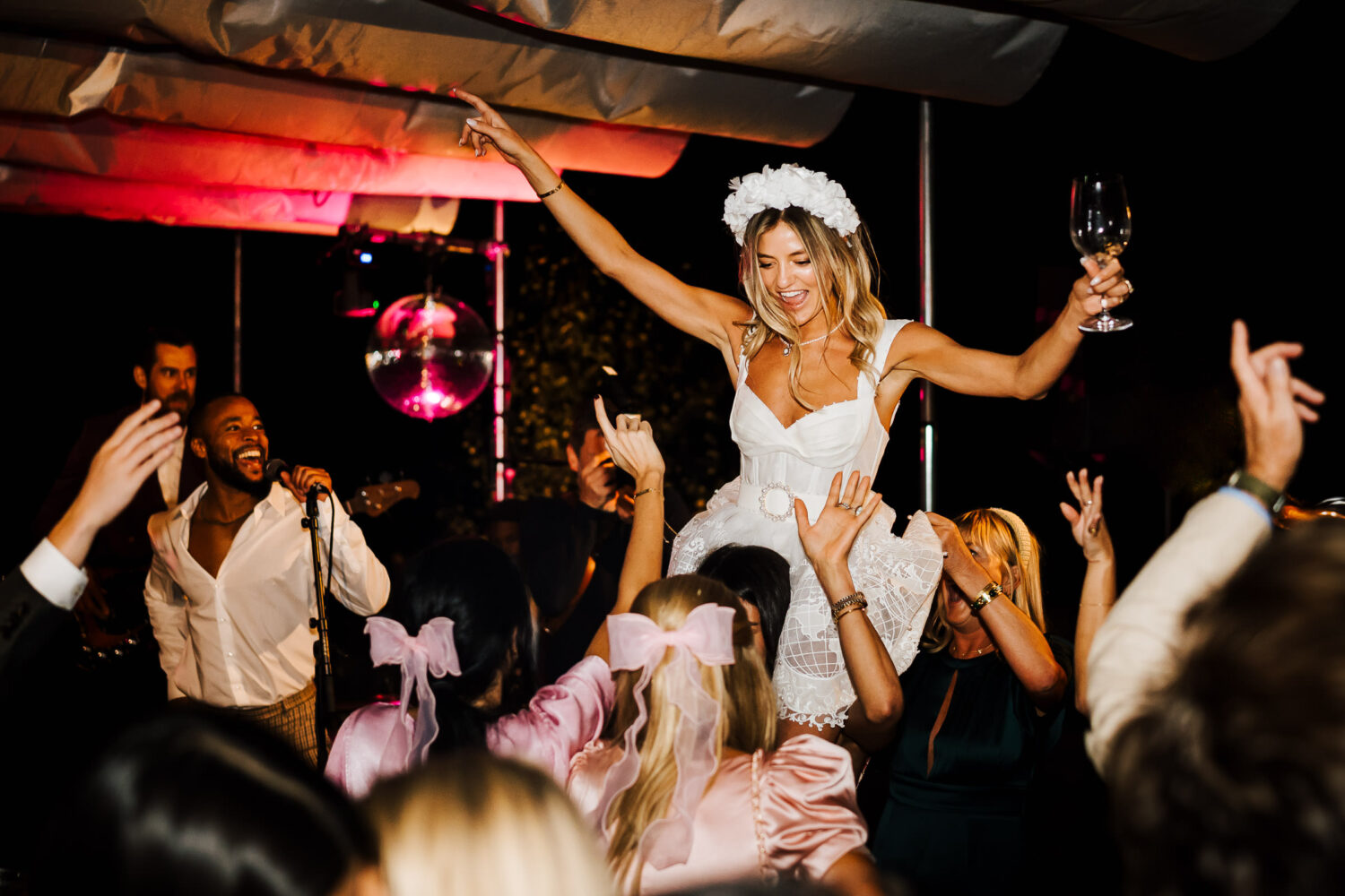 A bride in white being lifted on the crowds shoulders and dancing