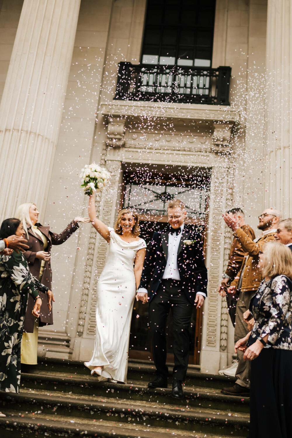 A bride and groom walking out of Old Marylebone Town Hall in London through a cloud of confetti