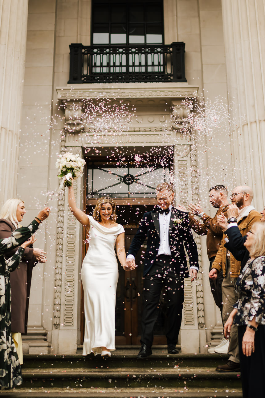 A newly married couple walking through confetti at Old Marylebone Town Hall